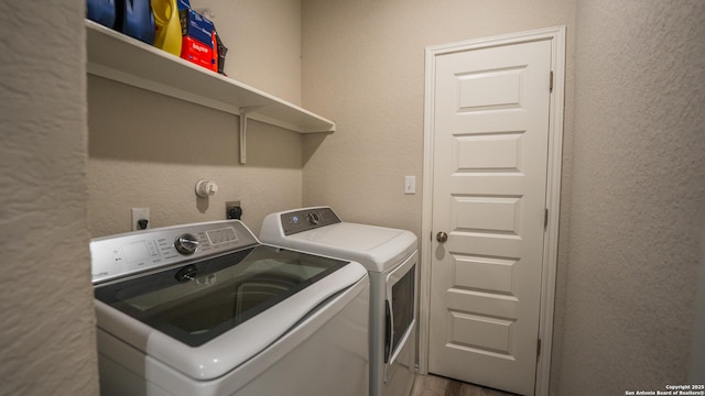 clothes washing area featuring washing machine and clothes dryer, a textured wall, wood finished floors, and laundry area