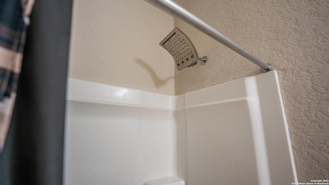 interior details with a textured wall and a shower