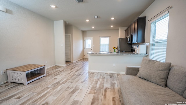 kitchen featuring recessed lighting, light stone counters, stainless steel appliances, light wood-style flooring, and open floor plan