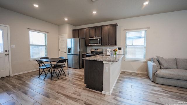 kitchen with stainless steel appliances, a sink, dark brown cabinetry, a peninsula, and light wood-style flooring