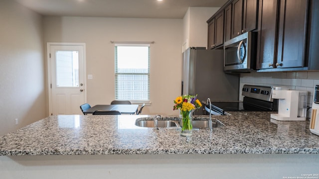 kitchen featuring dark brown cabinets, decorative backsplash, light stone countertops, and appliances with stainless steel finishes