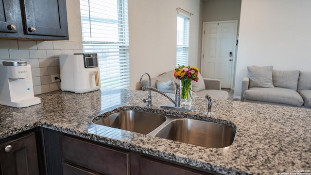 kitchen featuring dark stone countertops, dark brown cabinetry, decorative backsplash, and a sink