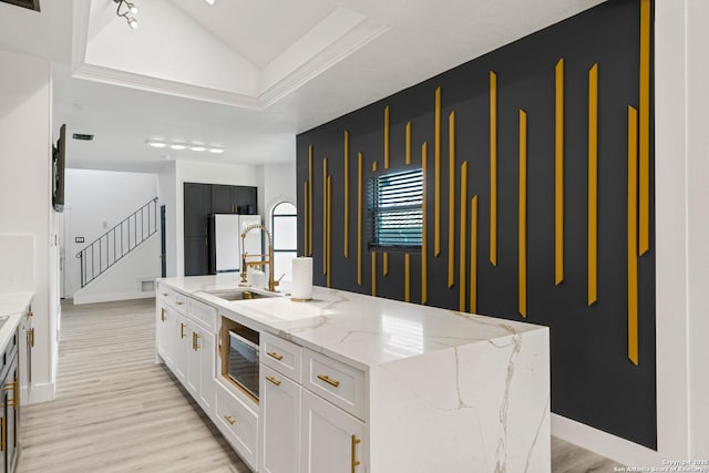 kitchen featuring a sink, stainless steel microwave, freestanding refrigerator, light wood-style floors, and white cabinetry