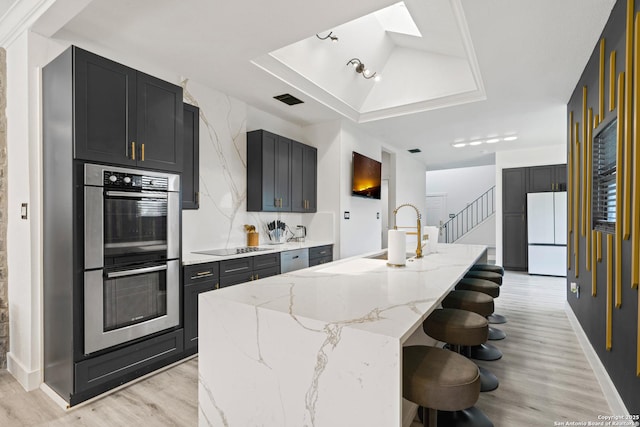 kitchen featuring stainless steel double oven, a raised ceiling, a sink, freestanding refrigerator, and light wood-style flooring