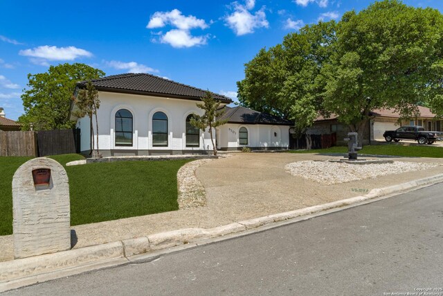 view of front of property with fence, a tiled roof, stucco siding, concrete driveway, and a front yard