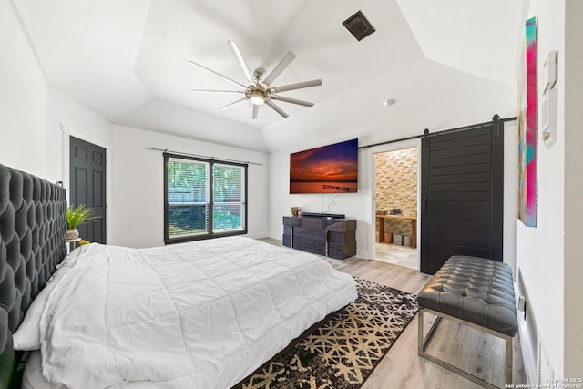 bedroom featuring a barn door, visible vents, a ceiling fan, wood finished floors, and a raised ceiling