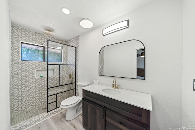 bathroom featuring a tile shower, toilet, vanity, and wood finished floors