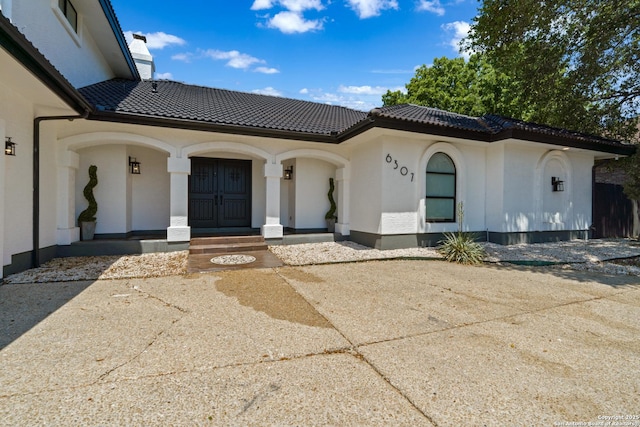 view of front of home with a tile roof, concrete driveway, a chimney, and stucco siding