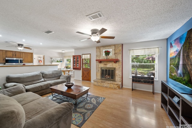 9416 Geronimo Vw, San Antonio, TX 78254 - living room featuring ceiling fan, a textured ceiling, light wood-style flooring, a fireplace, and baseboards