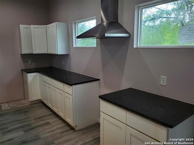 kitchen featuring white cabinets, dark countertops, wall chimney exhaust hood, and light wood finished floors