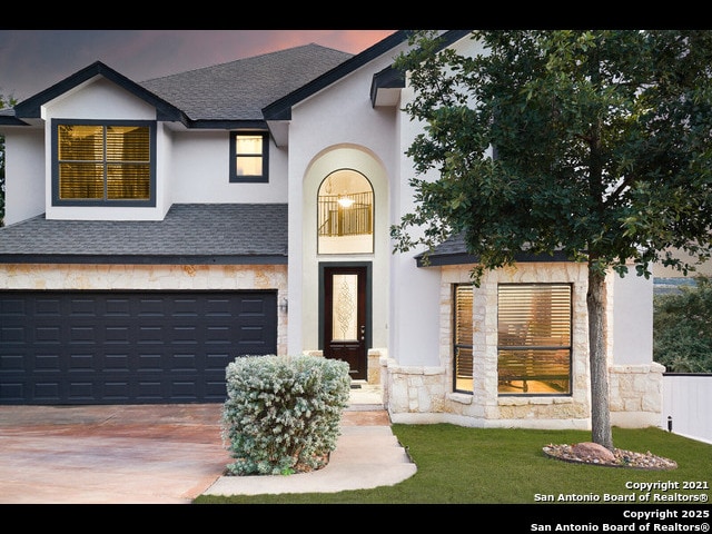 view of front of home featuring concrete driveway, stone siding, a shingled roof, an attached garage, and stucco siding