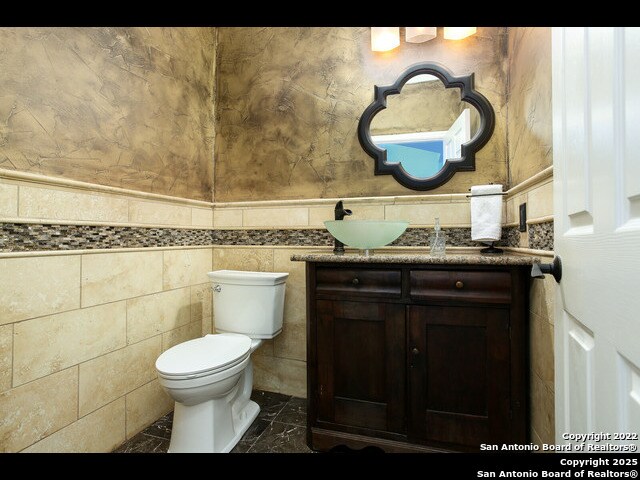 half bath featuring marble finish floor, toilet, vanity, and tile walls