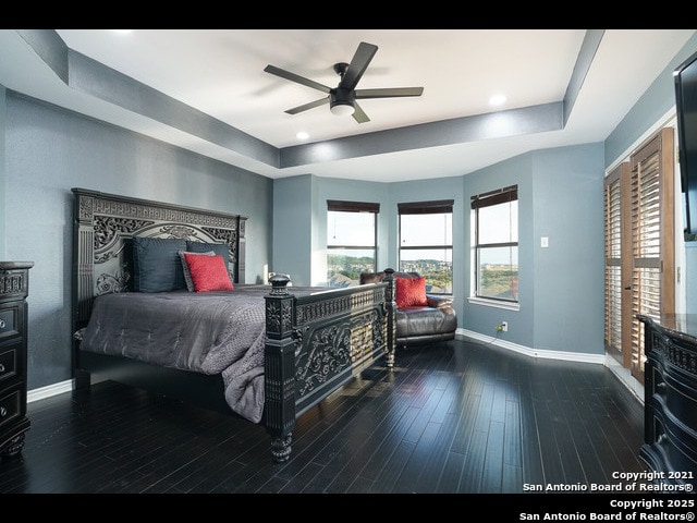 bedroom with wood-type flooring, baseboards, and a tray ceiling