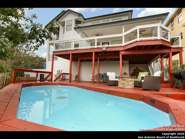 rear view of property with a fenced in pool, stucco siding, a patio area, a fire pit, and a deck