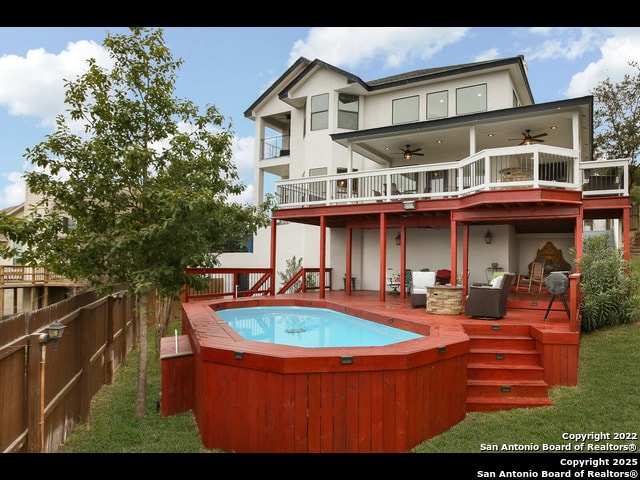 rear view of property with a balcony, fence, stucco siding, a wooden deck, and ceiling fan