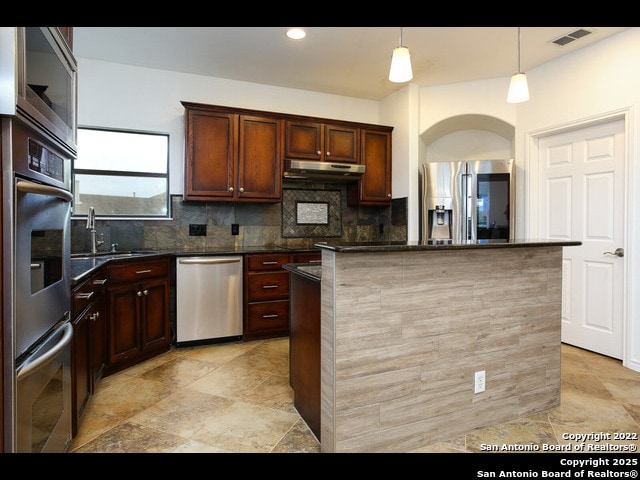 kitchen featuring arched walkways, a sink, decorative backsplash, under cabinet range hood, and appliances with stainless steel finishes