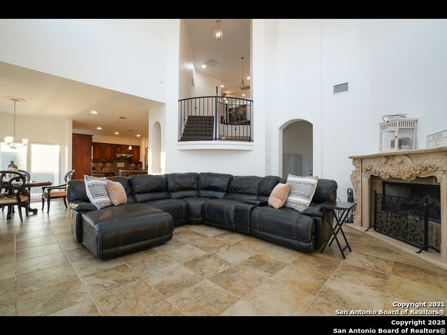 living room featuring arched walkways, an inviting chandelier, a towering ceiling, and a premium fireplace