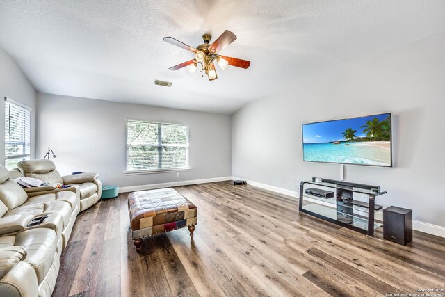 living room with a textured ceiling, visible vents, baseboards, wood finished floors, and ceiling fan