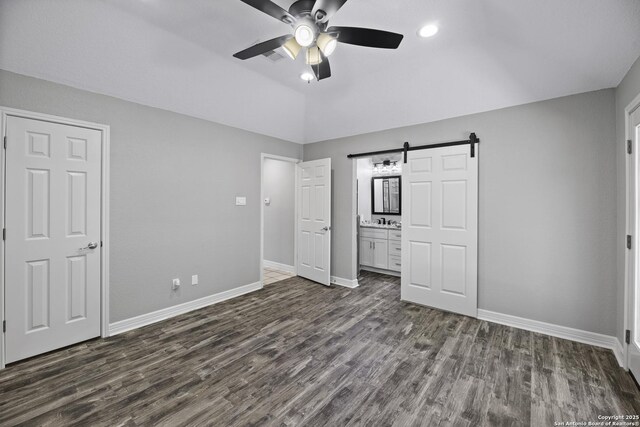 9400 Woodland Hls, San Antonio, TX 78250 - unfurnished bedroom featuring a barn door, connected bathroom, baseboards, and dark wood-style floors
