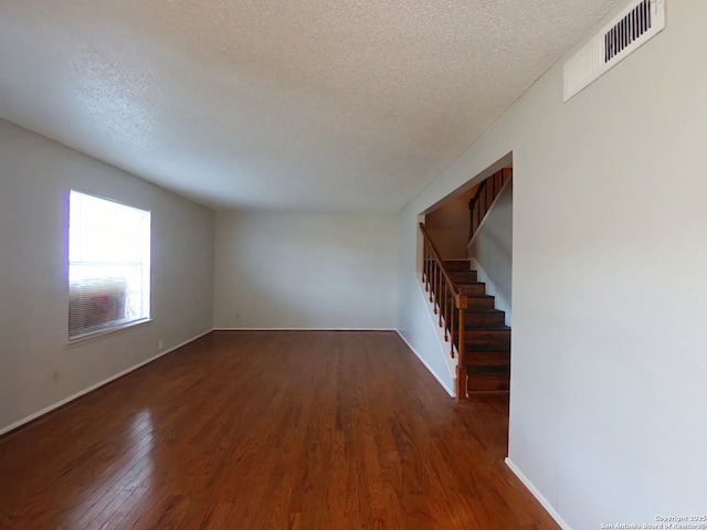 unfurnished room with stairway, wood finished floors, visible vents, baseboards, and a textured ceiling
