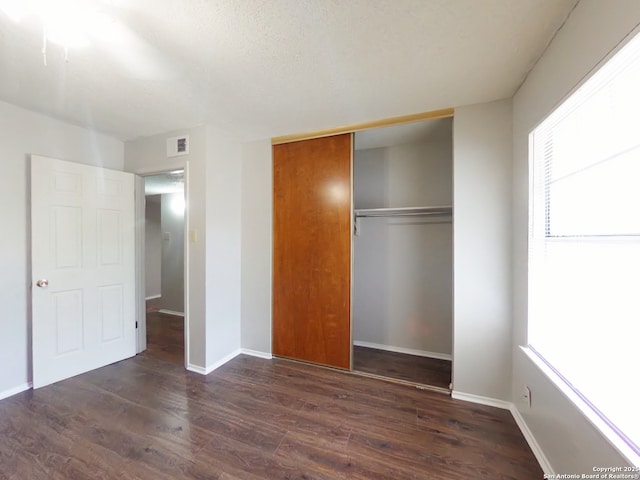 unfurnished bedroom featuring baseboards, wood finished floors, visible vents, and a closet