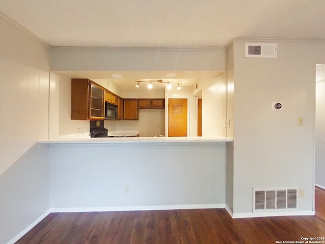 kitchen with black microwave, visible vents, wood finished floors, and brown cabinetry
