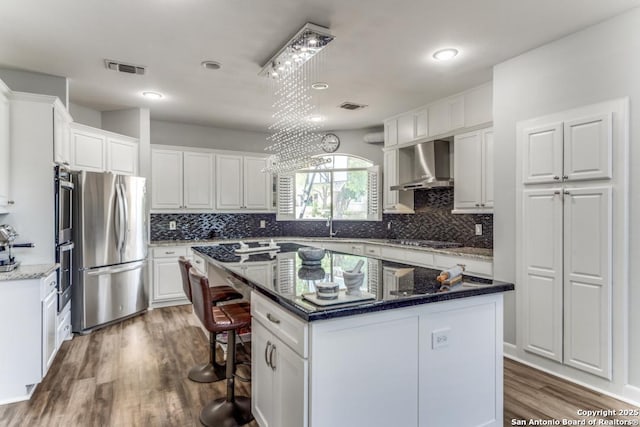 19111 Nature Oaks, San Antonio, TX 78258 - kitchen with stainless steel appliances, a kitchen bar, white cabinets, wall chimney exhaust hood, and a kitchen island