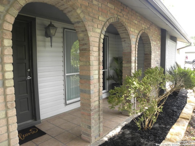 entrance to property featuring a porch and brick siding
