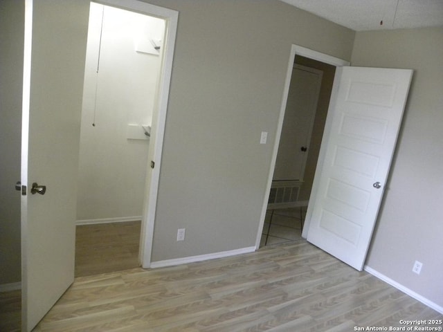 unfurnished bedroom with visible vents, light wood-style flooring, baseboards, and a spacious closet