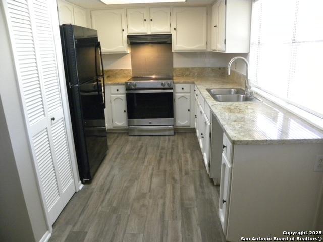kitchen with wood finished floors, a sink, freestanding refrigerator, electric stove, and under cabinet range hood