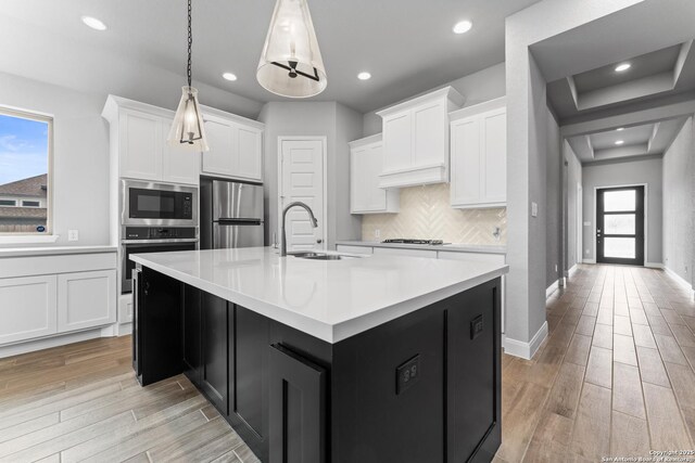kitchen featuring light wood finished floors, light countertops, a sink, decorative backsplash, and appliances with stainless steel finishes