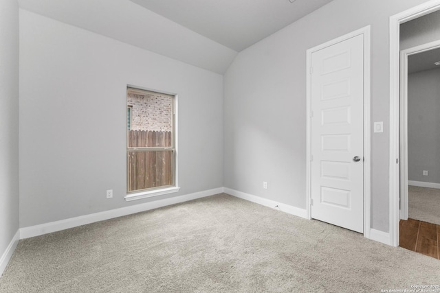 empty room featuring baseboards, vaulted ceiling, and carpet flooring
