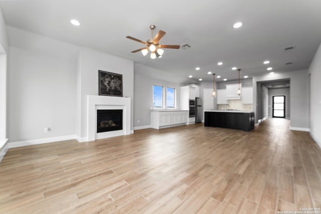 unfurnished living room featuring recessed lighting, baseboards, a fireplace, light wood-style flooring, and ceiling fan