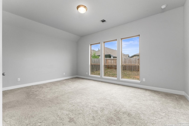 carpeted spare room featuring lofted ceiling, baseboards, and visible vents