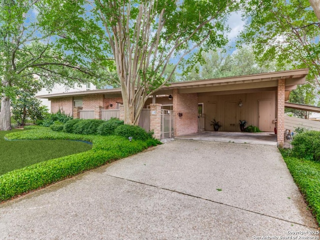 ranch-style home with a carport, driveway, brick siding, and fence