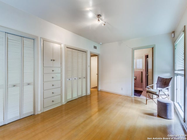 bedroom with ensuite bath, multiple closets, visible vents, and light wood-style floors