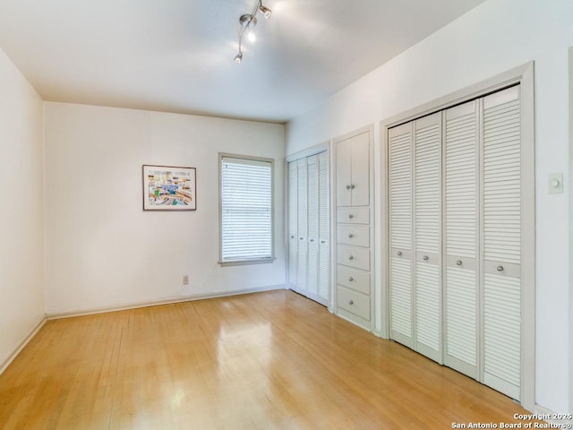 unfurnished bedroom featuring light wood-type flooring, multiple closets, and baseboards