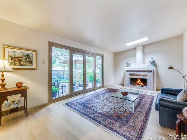 living area with wood finished floors, a skylight, a lit fireplace, and french doors