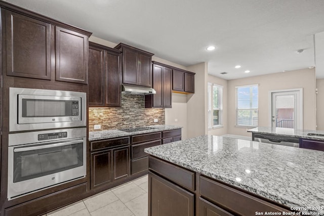 kitchen featuring light stone counters, under cabinet range hood, backsplash, and stainless steel appliances
