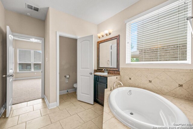 full bathroom with visible vents, toilet, vanity, baseboards, and a garden tub