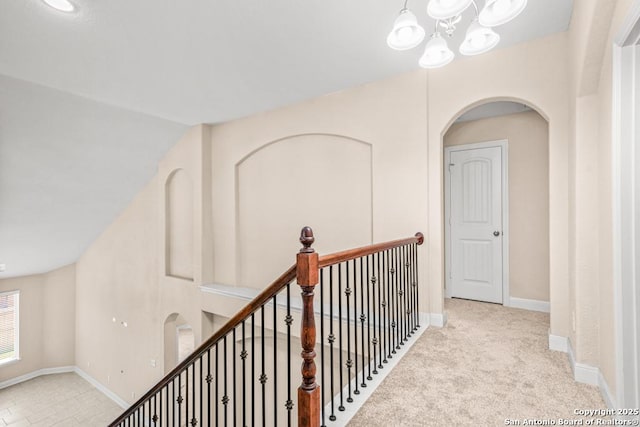 corridor with an upstairs landing, arched walkways, baseboards, a notable chandelier, and carpet flooring