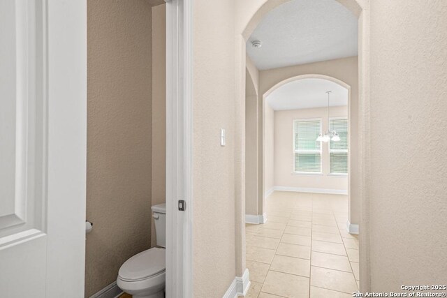 bathroom with a textured wall, baseboards, tile patterned flooring, and toilet