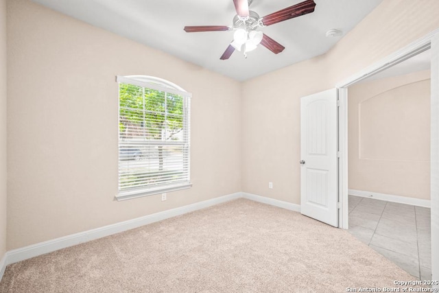 carpeted empty room featuring a ceiling fan, baseboards, and tile patterned floors