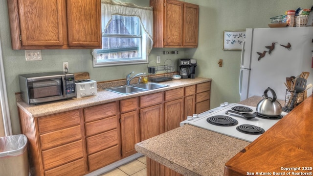 kitchen with stainless steel microwave, freestanding refrigerator, brown cabinets, and a sink