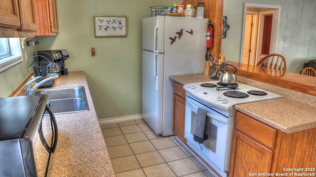 kitchen with a sink, brown cabinetry, white appliances, light tile patterned floors, and light countertops