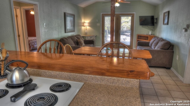 interior space featuring open floor plan, vaulted ceiling, a ceiling fan, a textured wall, and light tile patterned floors