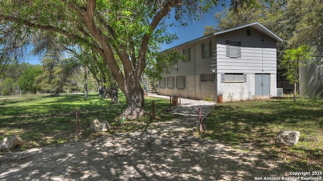 view of property exterior with brick siding, cooling unit, a lawn, and stairway