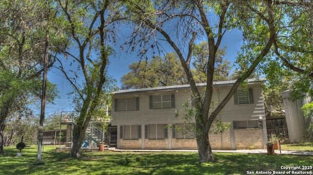 exterior space with brick siding, a front lawn, stairs, and fence