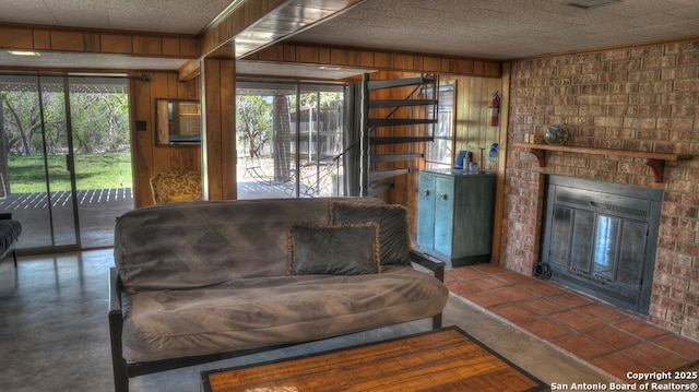 living room featuring a brick fireplace, wood walls, a textured ceiling, and concrete floors