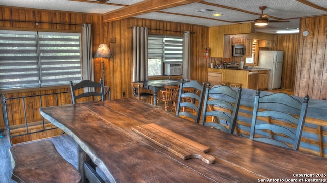 dining room with a ceiling fan, a textured ceiling, wooden walls, and visible vents